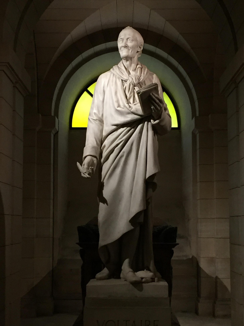 伏尔泰的棺木前面耸立着他的全身雕像,右手捏着鹅毛笔,左手拿着一卷